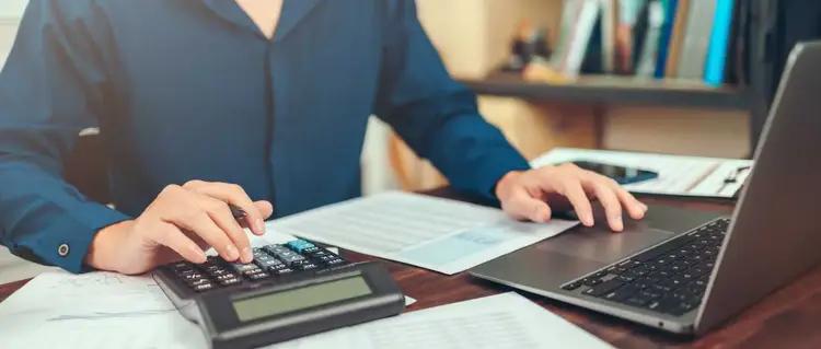 A person is typing on a calculator on a desk.